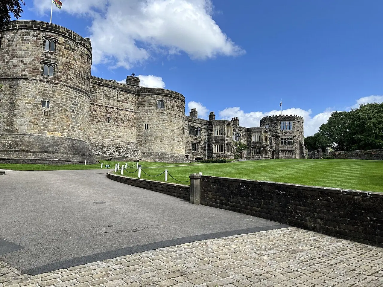Stone walls and towers of Skipton Castle beside its lawn
